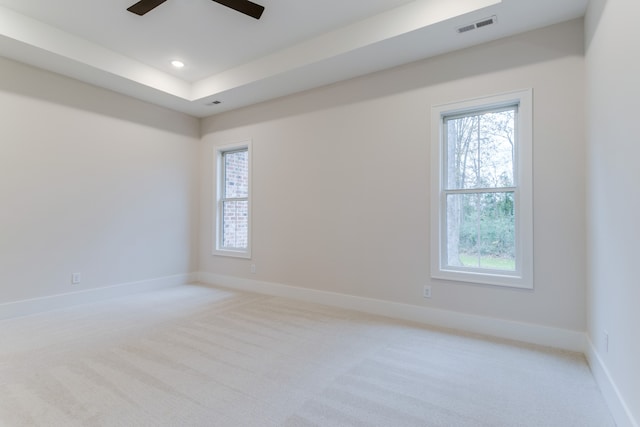 empty room featuring ceiling fan, a raised ceiling, and light carpet