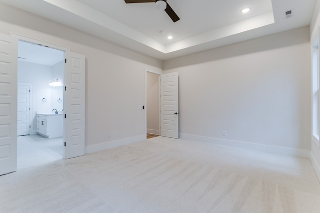 unfurnished bedroom featuring ensuite bathroom, a raised ceiling, sink, ceiling fan, and light colored carpet