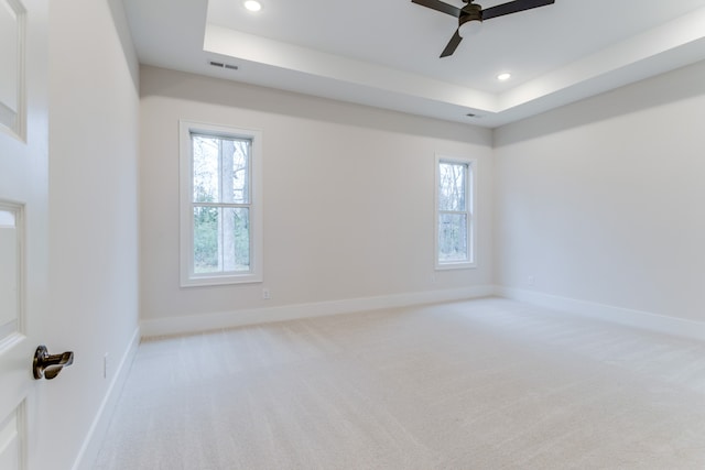 unfurnished room with light colored carpet, a raised ceiling, plenty of natural light, and ceiling fan