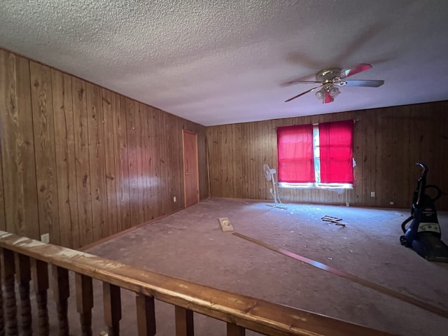 spare room featuring a textured ceiling, wood walls, and ceiling fan