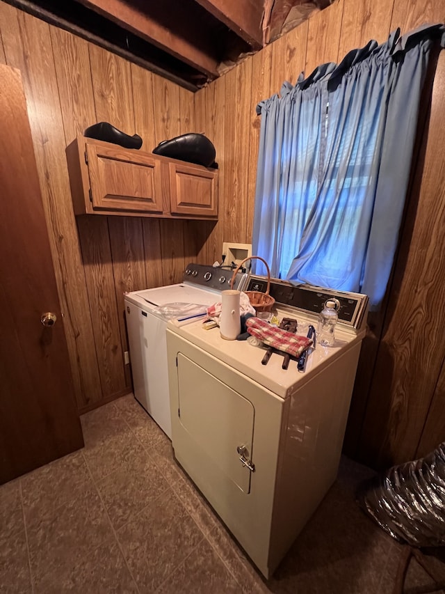 laundry area with wooden walls, independent washer and dryer, dark tile patterned floors, and cabinets