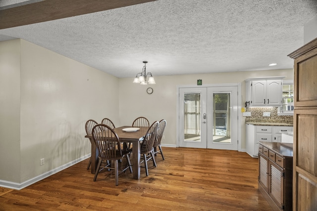 dining room with dark wood-type flooring, a notable chandelier, french doors, and a textured ceiling