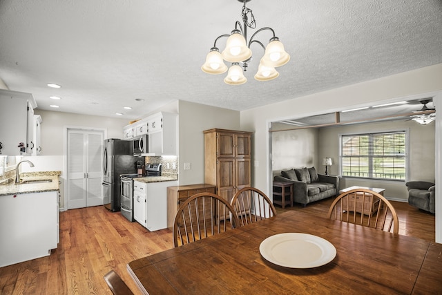 dining area featuring a textured ceiling, sink, light wood-type flooring, and ceiling fan with notable chandelier