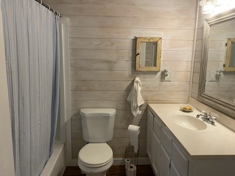 full bathroom with vanity, wooden walls, toilet, and shower / bathtub combination with curtain