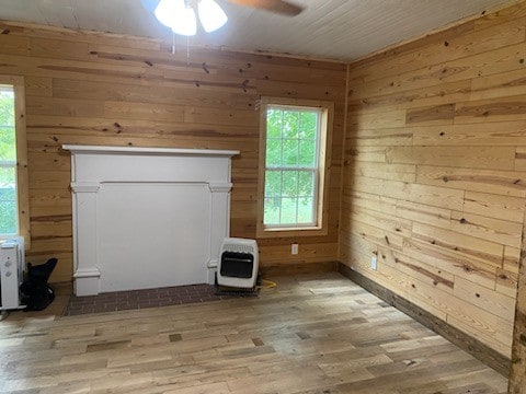 interior space featuring light wood-type flooring, wooden walls, ceiling fan, and heating unit