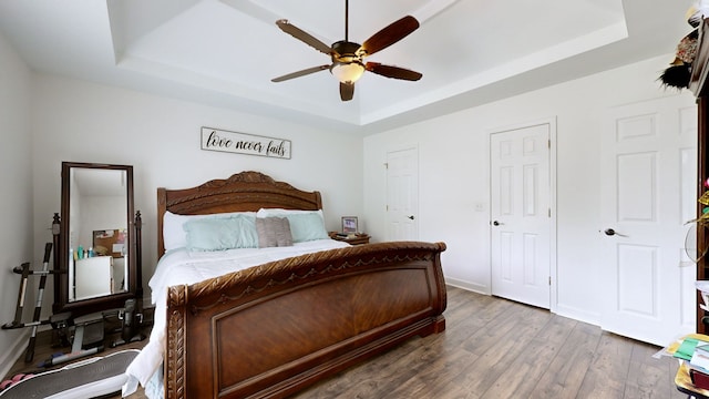 bedroom featuring ceiling fan, a raised ceiling, and dark wood-type flooring