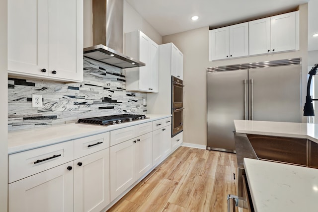 kitchen featuring light hardwood / wood-style floors, tasteful backsplash, white cabinets, wall chimney exhaust hood, and stainless steel appliances