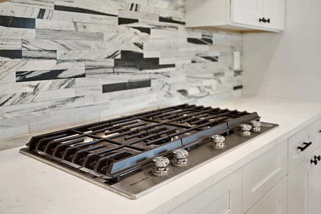 interior details with stainless steel gas stovetop, white cabinetry, and tasteful backsplash