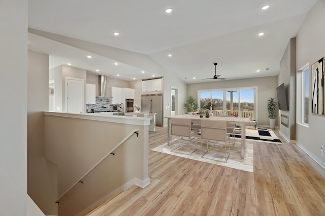 kitchen with light hardwood / wood-style flooring, wall chimney exhaust hood, white cabinetry, stainless steel appliances, and vaulted ceiling