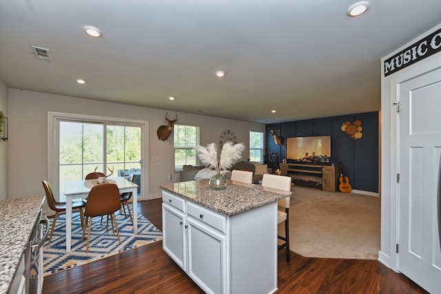 kitchen with light stone counters, a kitchen island, white cabinetry, dark hardwood / wood-style floors, and a breakfast bar area