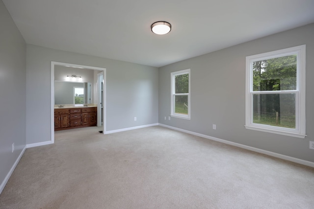 unfurnished bedroom with light carpet, ensuite bathroom, and multiple windows