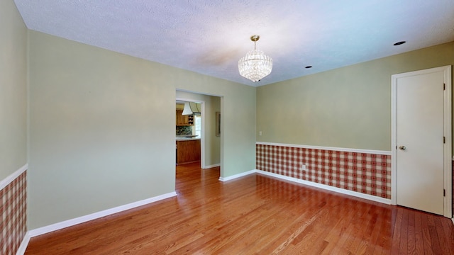 spare room featuring wood-type flooring, a notable chandelier, and a textured ceiling