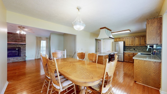 dining room with a stone fireplace, sink, light hardwood / wood-style flooring, and ceiling fan