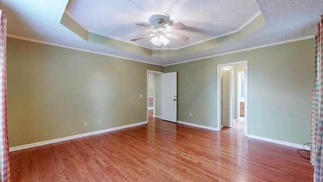 empty room featuring light wood-type flooring, a tray ceiling, ceiling fan, and crown molding