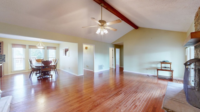 living room featuring a textured ceiling, a fireplace, vaulted ceiling with beams, hardwood / wood-style floors, and ceiling fan