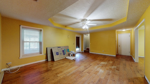 empty room featuring a textured ceiling, a raised ceiling, hardwood / wood-style floors, and ceiling fan