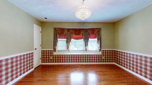 unfurnished room featuring a textured ceiling, hardwood / wood-style floors, and a chandelier