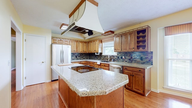 kitchen featuring light hardwood / wood-style floors, backsplash, exhaust hood, a center island, and sink