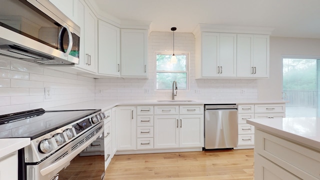 kitchen featuring appliances with stainless steel finishes, a healthy amount of sunlight, sink, and decorative light fixtures