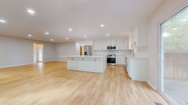 kitchen featuring sink, a kitchen island, white cabinetry, stainless steel appliances, and light wood-type flooring