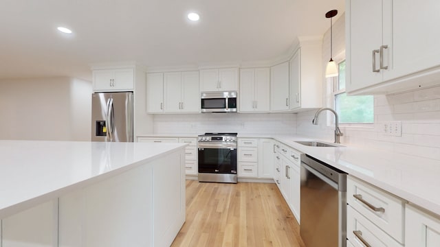 kitchen with appliances with stainless steel finishes, white cabinets, pendant lighting, light hardwood / wood-style flooring, and sink