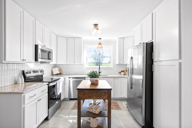 kitchen with stainless steel appliances, hanging light fixtures, light tile patterned floors, and white cabinetry