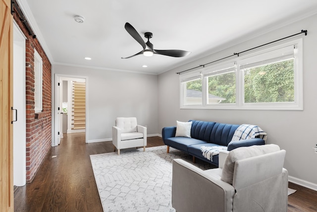 living room featuring ceiling fan, brick wall, dark wood-type flooring, crown molding, and a barn door