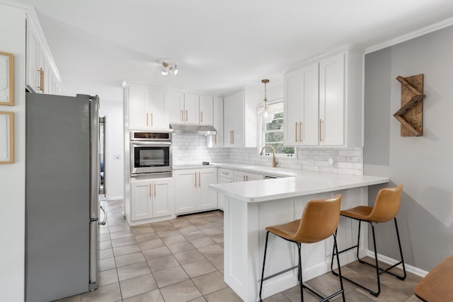 kitchen featuring appliances with stainless steel finishes, white cabinets, backsplash, kitchen peninsula, and a breakfast bar area