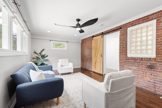 living room with brick wall, hardwood / wood-style flooring, crown molding, and a barn door