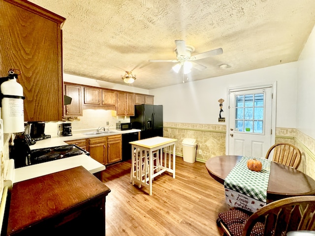 kitchen with tile walls, light wood-type flooring, black appliances, a textured ceiling, and ceiling fan