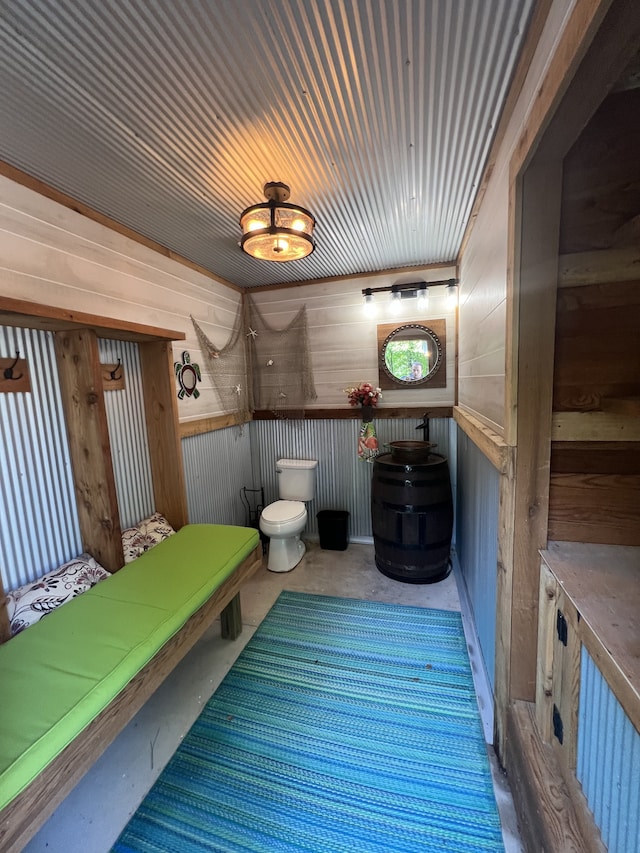 bathroom with concrete flooring, wood walls, and toilet