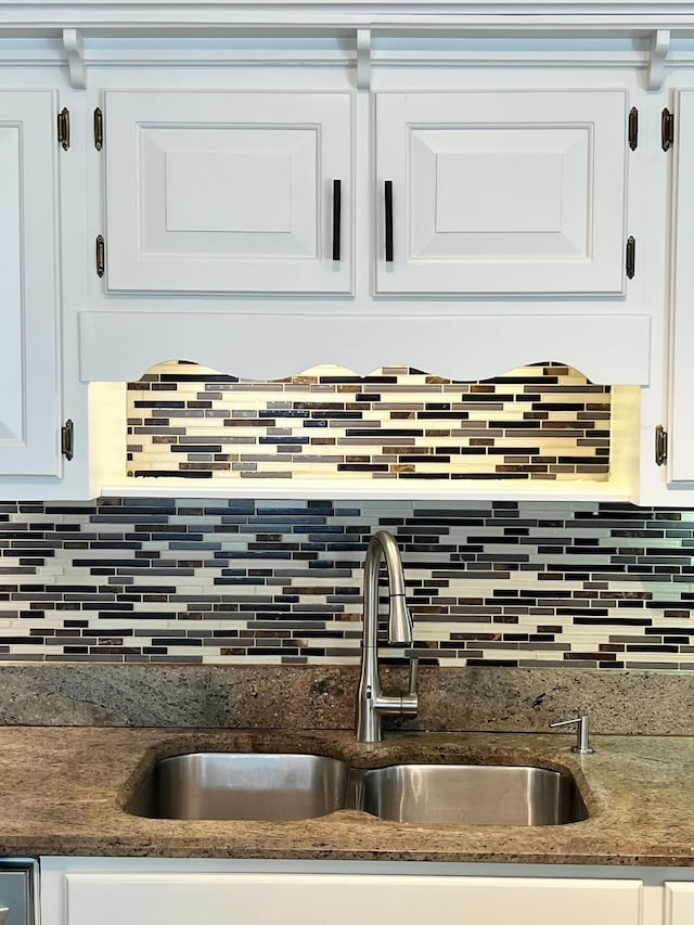 interior details featuring dark stone countertops, white cabinets, backsplash, and sink