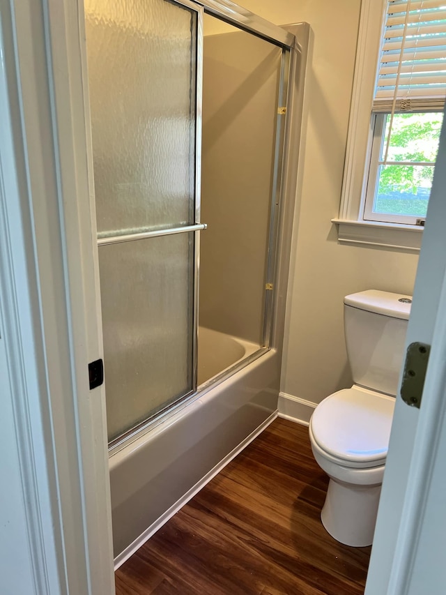 bathroom with combined bath / shower with glass door, hardwood / wood-style flooring, and toilet