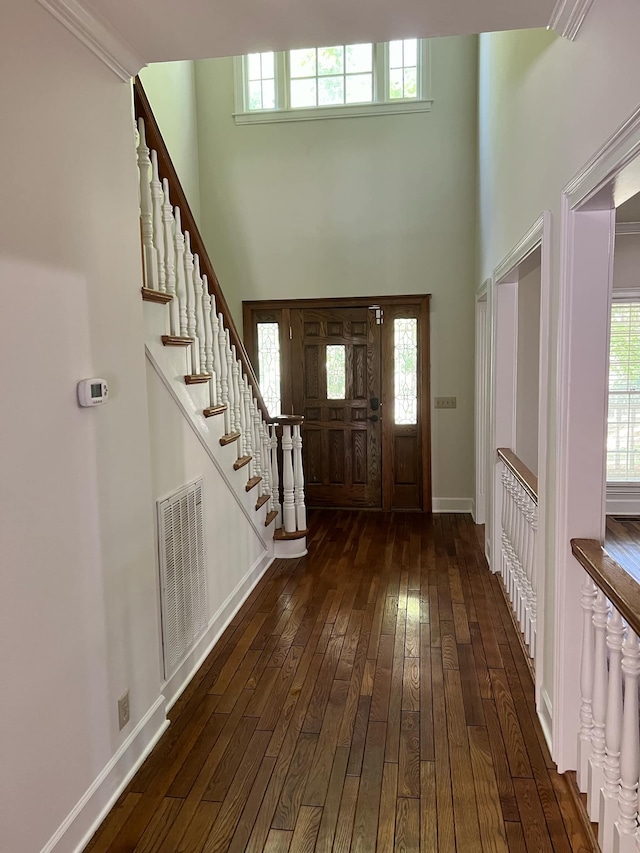 foyer with a towering ceiling, dark hardwood / wood-style floors, ornamental molding, and a healthy amount of sunlight