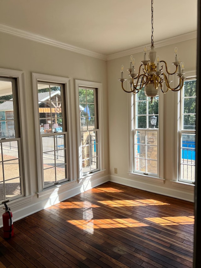 unfurnished dining area with ornamental molding, an inviting chandelier, dark wood-type flooring, and a healthy amount of sunlight