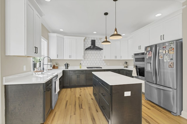 kitchen with pendant lighting, wall chimney exhaust hood, appliances with stainless steel finishes, a center island, and light wood-type flooring