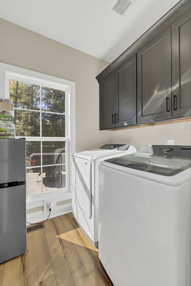 laundry room with separate washer and dryer, cabinets, and light hardwood / wood-style flooring