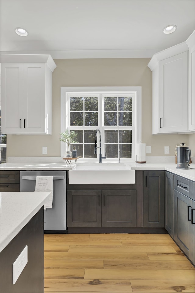 kitchen with sink, light hardwood / wood-style flooring, stainless steel dishwasher, and white cabinetry