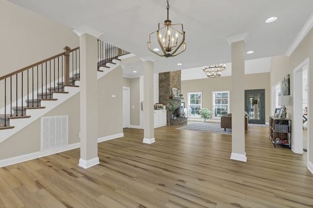 entryway featuring ornate columns, ornamental molding, a fireplace, and light hardwood / wood-style floors