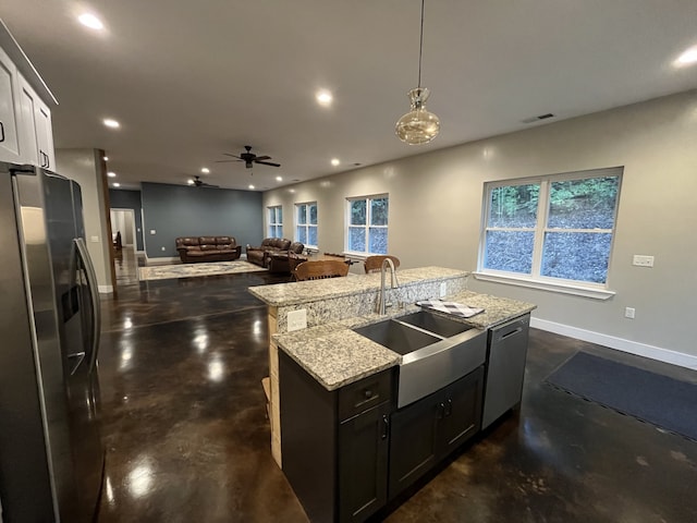 kitchen with sink, an island with sink, hanging light fixtures, appliances with stainless steel finishes, and light stone countertops