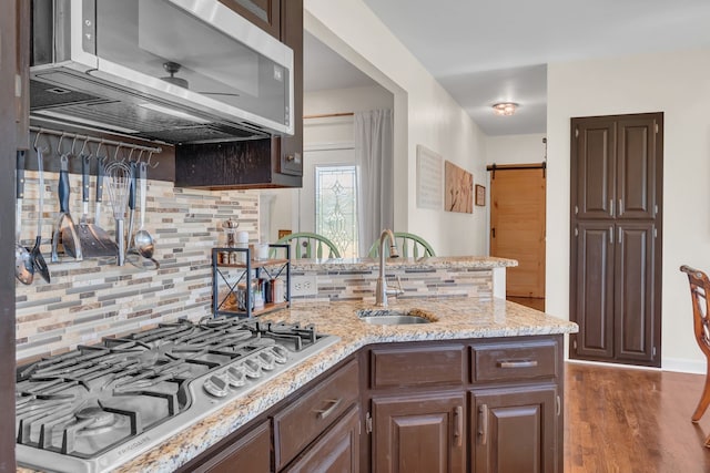 kitchen with tasteful backsplash, sink, dark wood-type flooring, a barn door, and appliances with stainless steel finishes