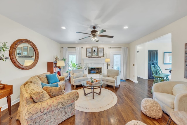 living room featuring dark hardwood / wood-style floors, ceiling fan, a premium fireplace, and a wealth of natural light