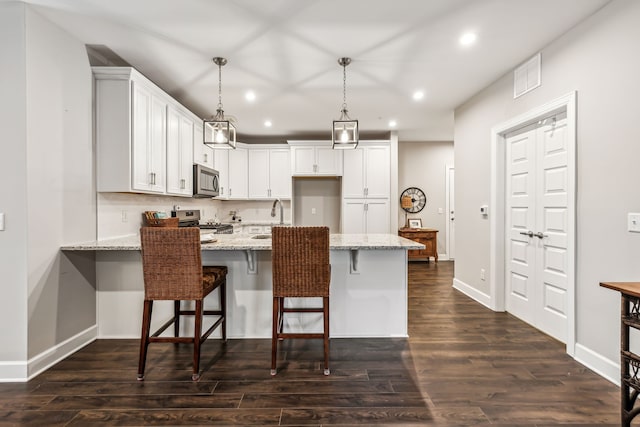 kitchen featuring white cabinetry, light stone counters, pendant lighting, stainless steel appliances, and a kitchen bar