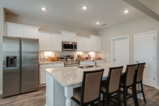 kitchen with appliances with stainless steel finishes, dark wood-type flooring, sink, a center island with sink, and white cabinetry