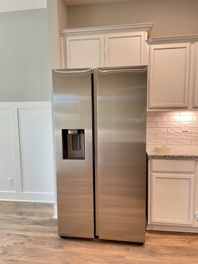 kitchen with white cabinets, stainless steel refrigerator with ice dispenser, light wood-type flooring, tasteful backsplash, and light stone counters