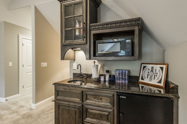 bar with dark stone countertops, vaulted ceiling, black microwave, sink, and light colored carpet