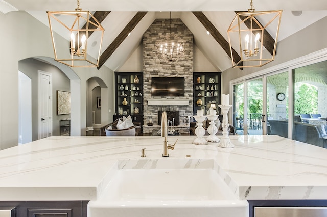 kitchen featuring a stone fireplace, a kitchen island with sink, hanging light fixtures, and sink