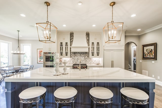 kitchen with custom exhaust hood, decorative light fixtures, light wood-type flooring, and a large island