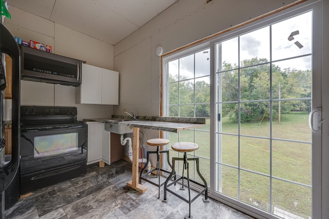 kitchen with white cabinets, black range with electric cooktop, exhaust hood, and a breakfast bar area