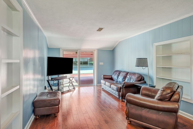 living room featuring built in shelves, a textured ceiling, hardwood / wood-style flooring, crown molding, and vaulted ceiling